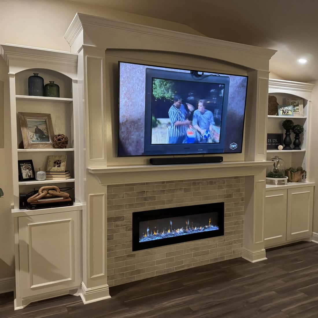 A built-in wall unit with arched shelves either side of a television and a linear fireplace.