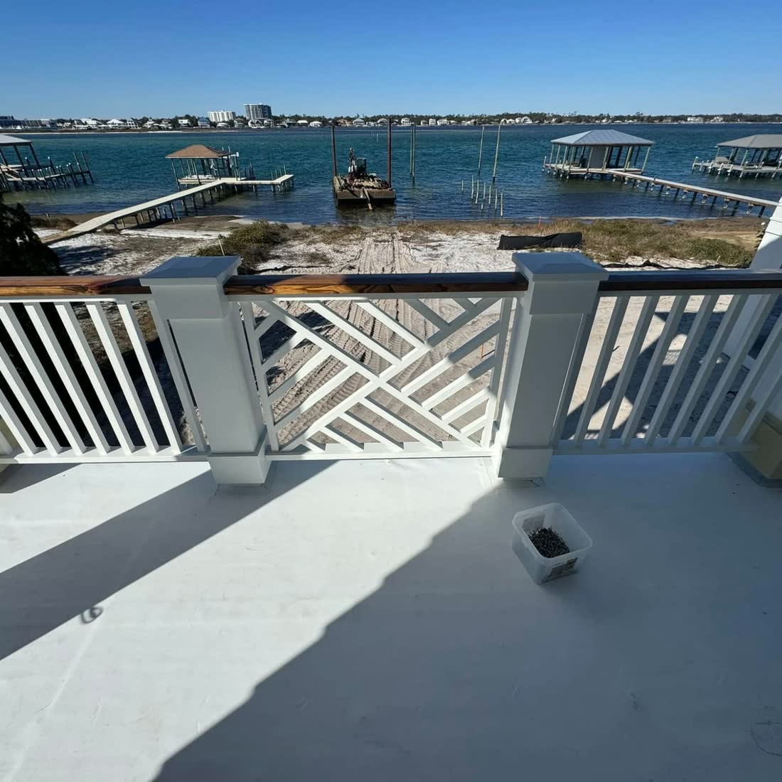 A white balcony railing with a chippendale panel and a wood cap rail, looking out over the bay.