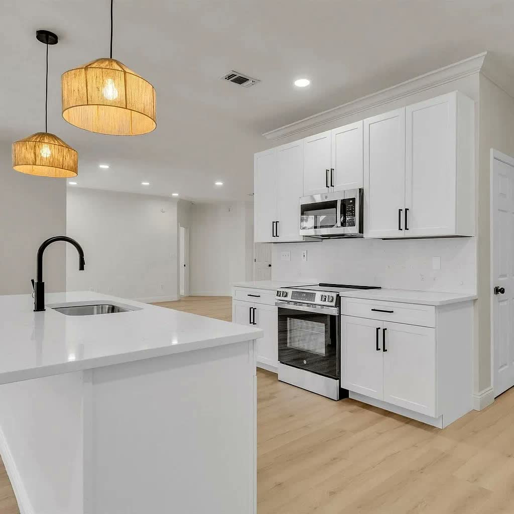 A remodeled white kitchen with two woven pendant lights over the island, shaker cabinets and a stainless range.