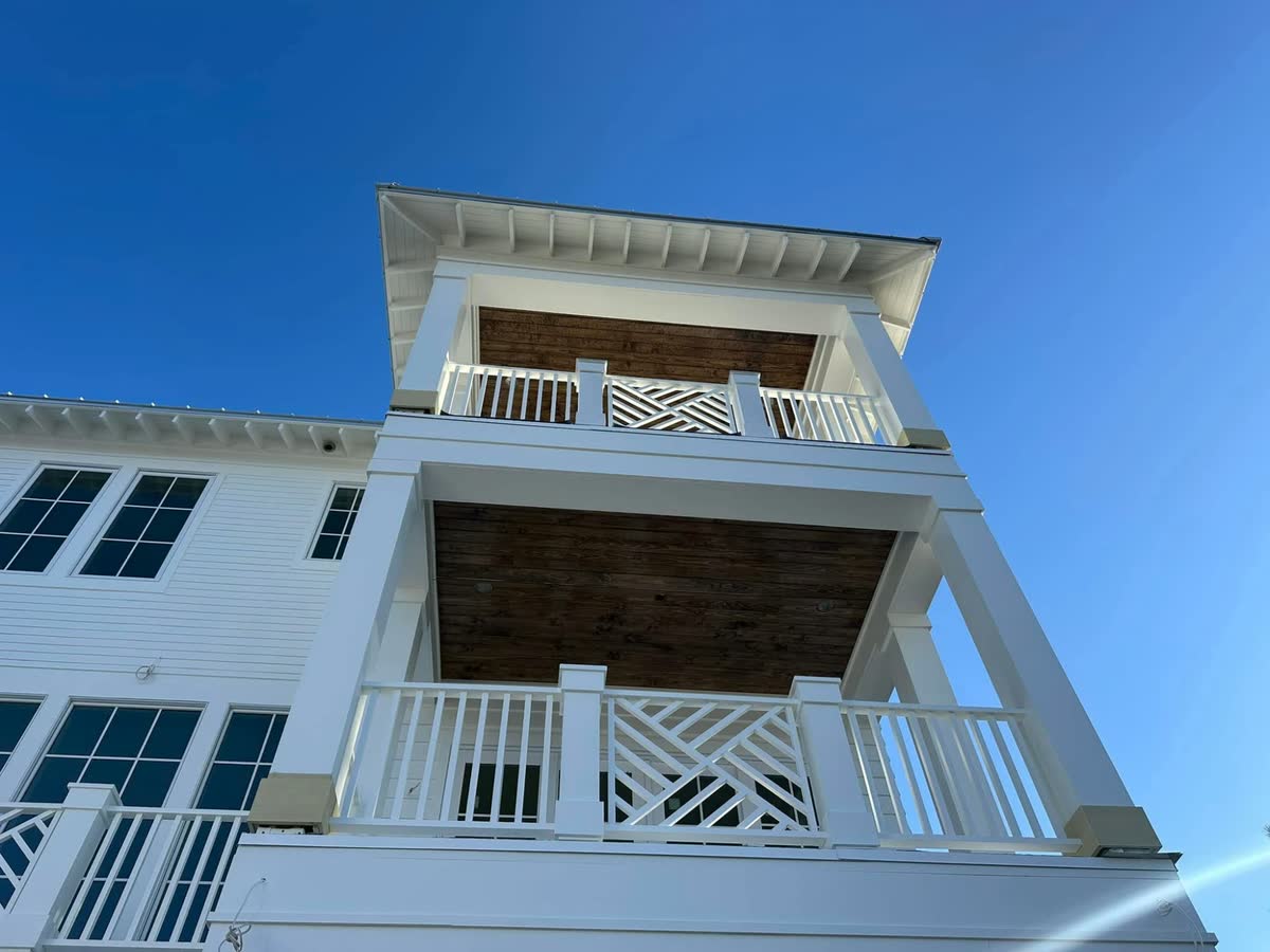 Looking up at two stacked porches with wood-planked ceilings and chippendale railings.