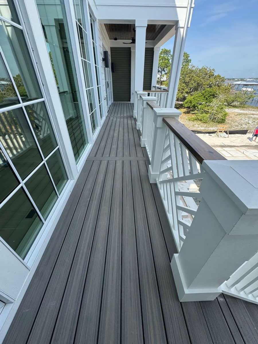 A long grey-board deck along a wall of windows, a white railing with a wood cap.