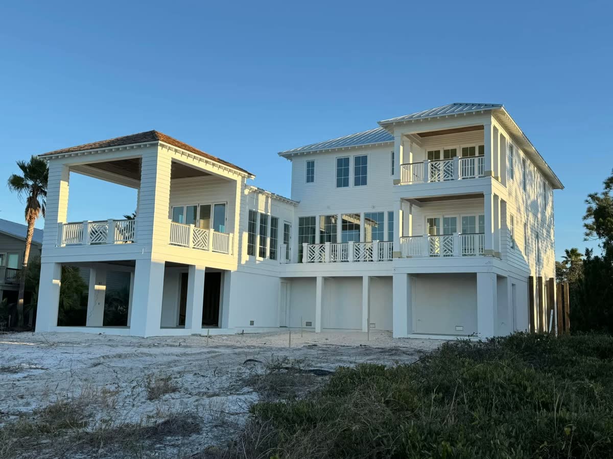 A large white raised beach house with stacked porches and white railings, seen from the beach at sunset.