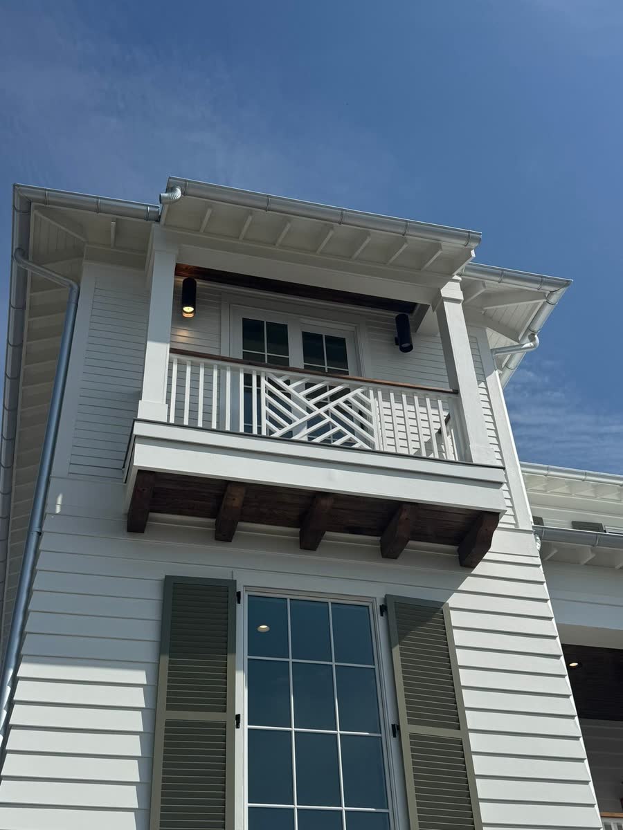 A small balcony with a chippendale railing on the upper floor of a white house.