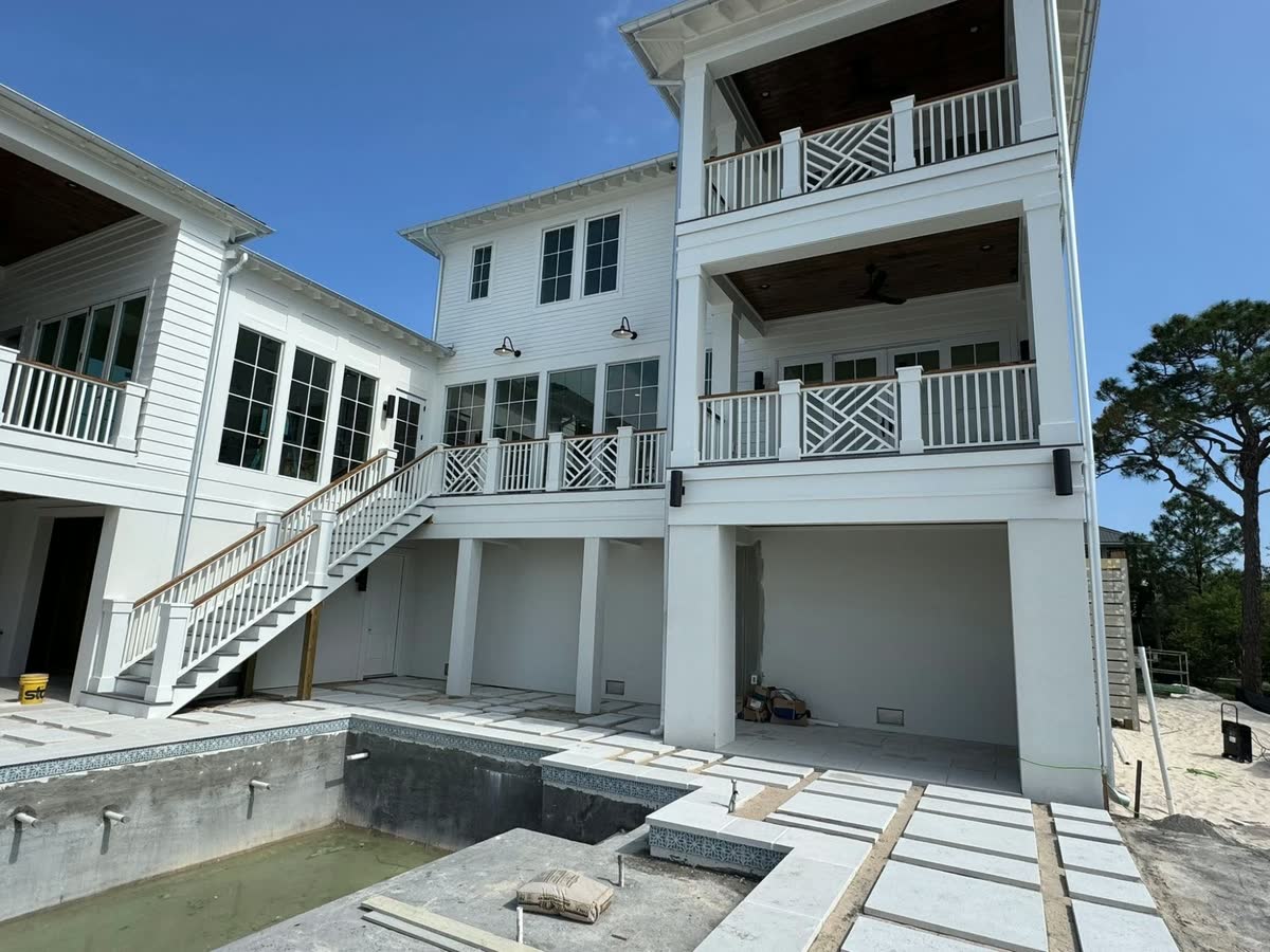 The back of a white raised house with stacked porches, a stair down to a pool being built.