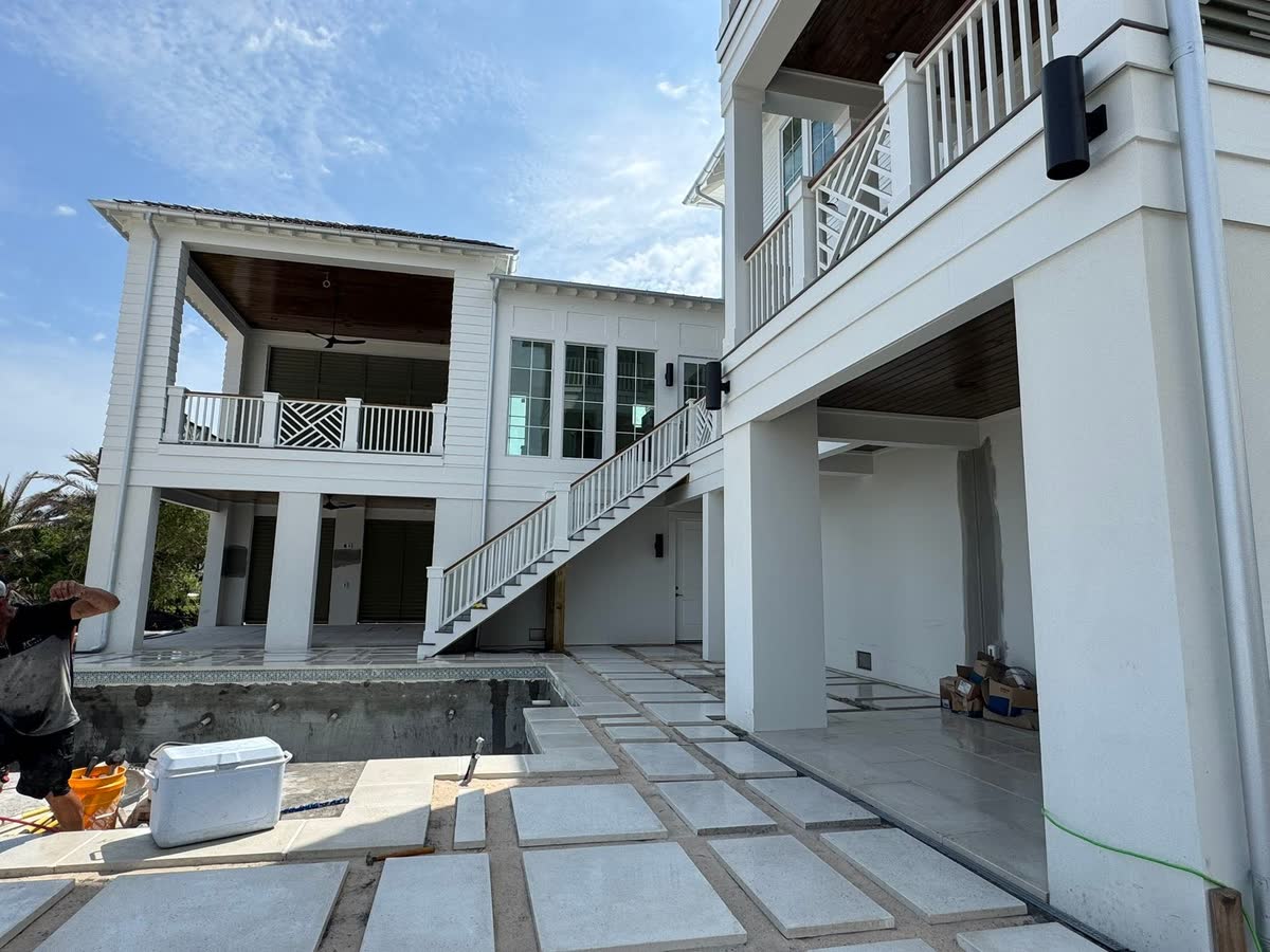 White porches and a stair at the back of a raised house, square pavers laid below.