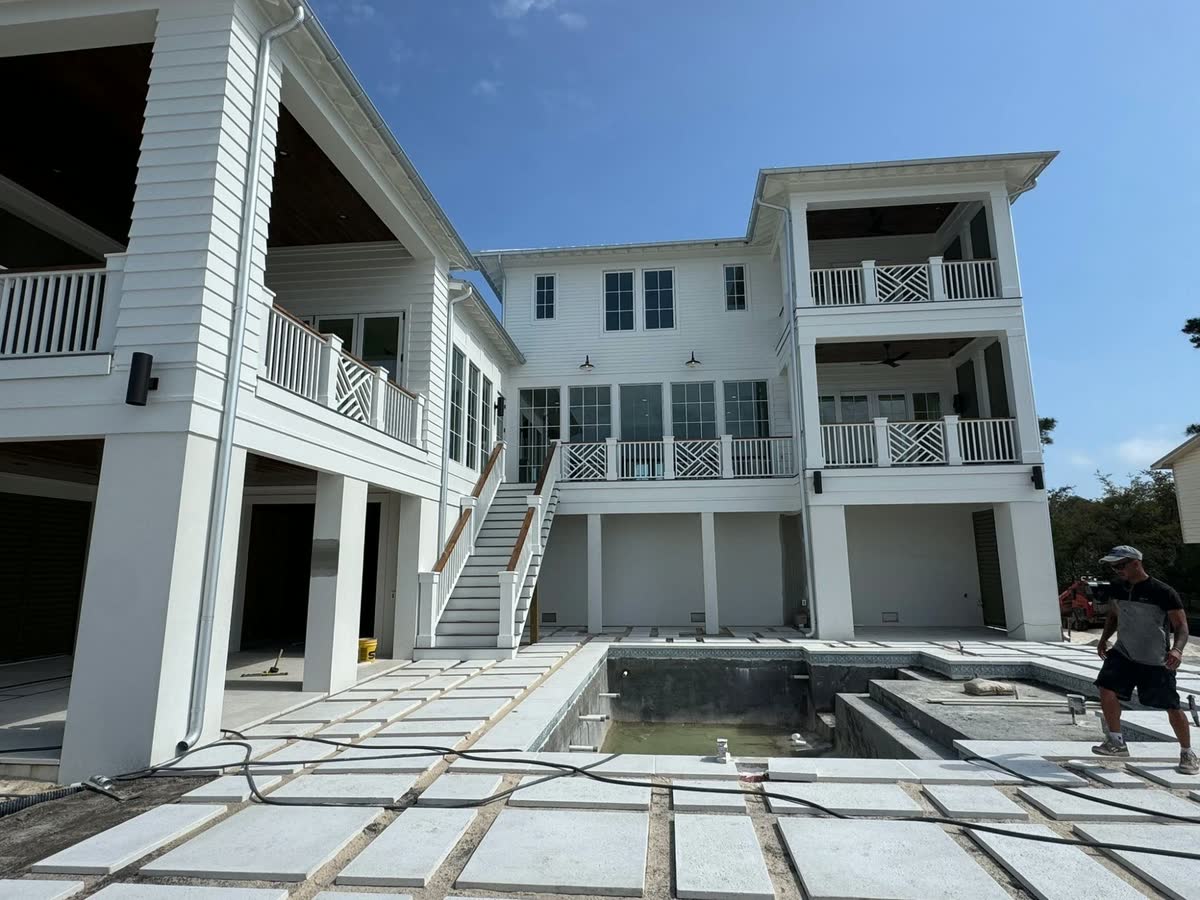 The back of a large white raised house with porches and a stair down to a new pool deck.