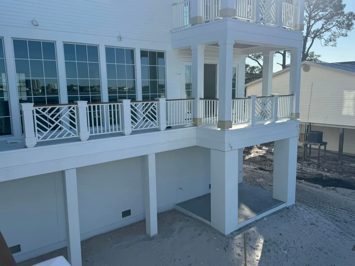 A long side deck with white posts and chippendale panels, the bay reflected in the windows.