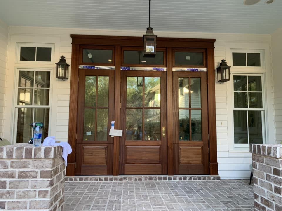 Double wood front doors with glass panes, transoms and lanterns on a brick porch.