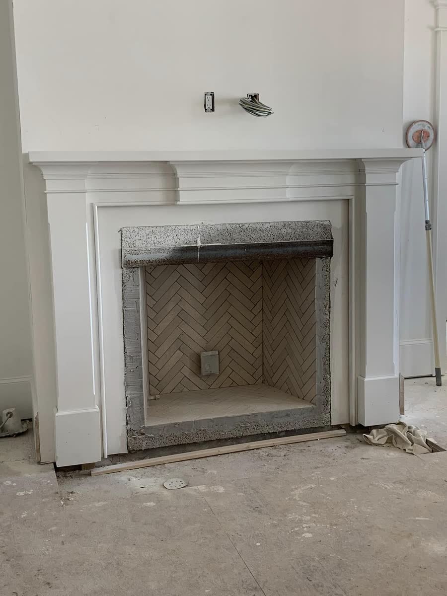 A white fireplace surround with a simple mantel, before the room is finished.