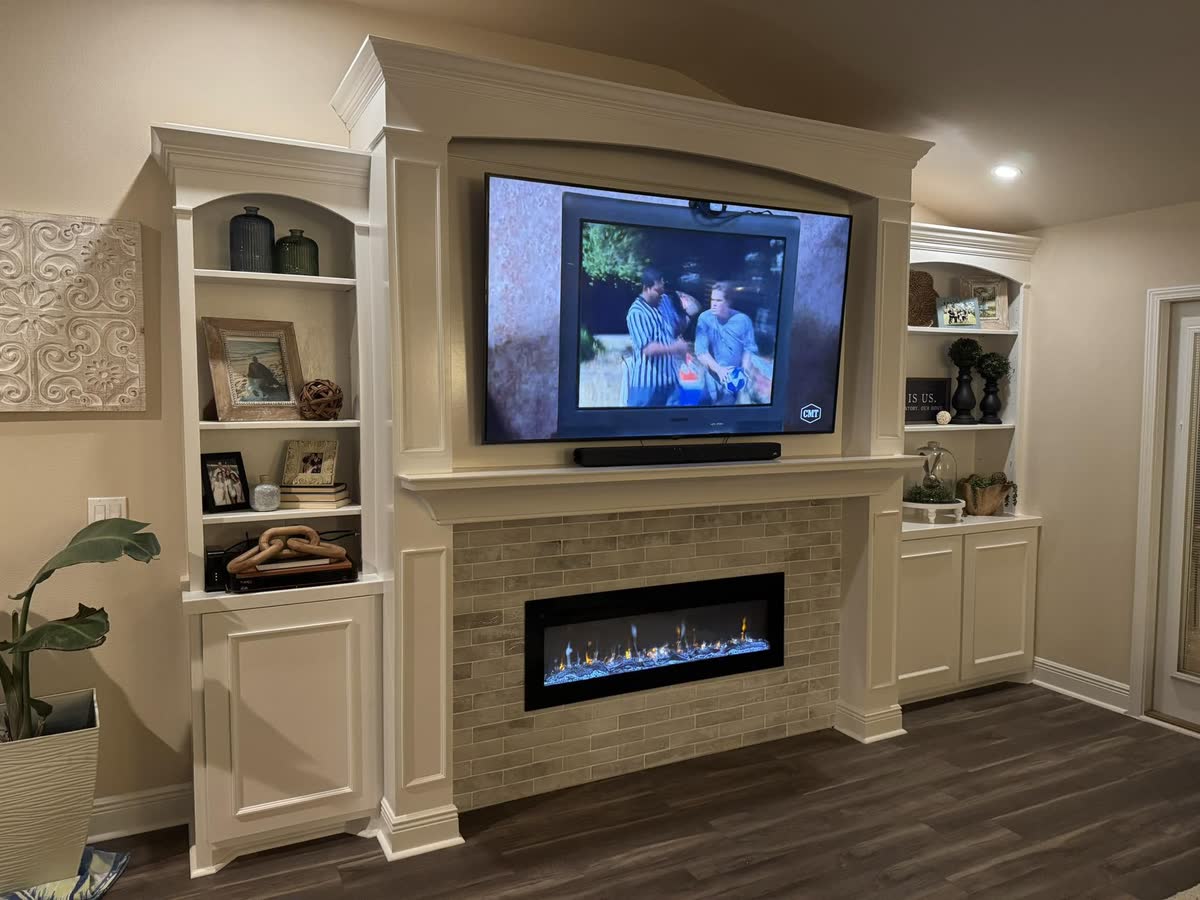 A built-in wall unit with arched shelves either side of a television and a linear fireplace.