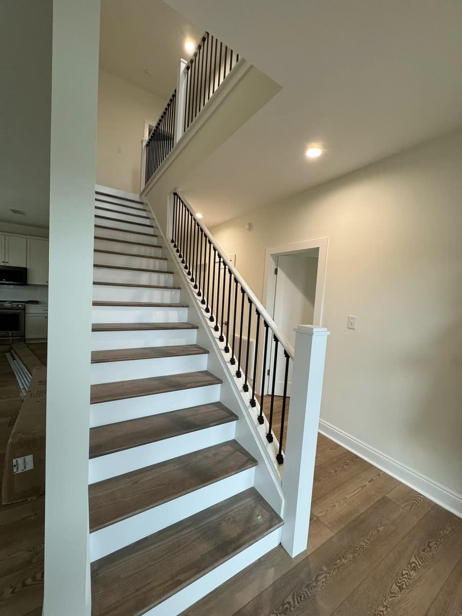 A stair with a wood handrail and black balusters climbing to an upper floor.