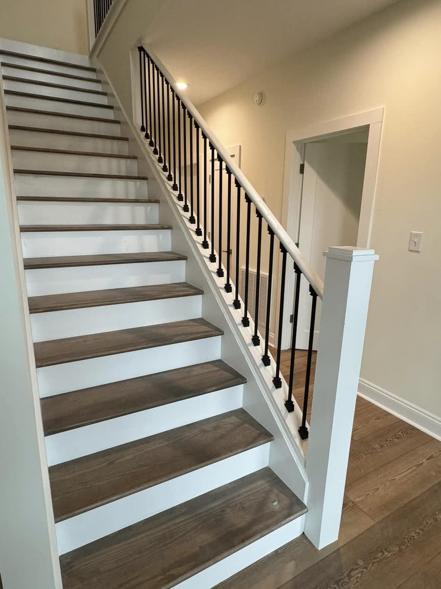 A staircase with white risers, wood treads and black metal balusters.