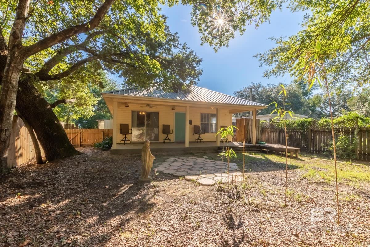 The back of a new cottage with a covered porch, a young garden and a wood fence.