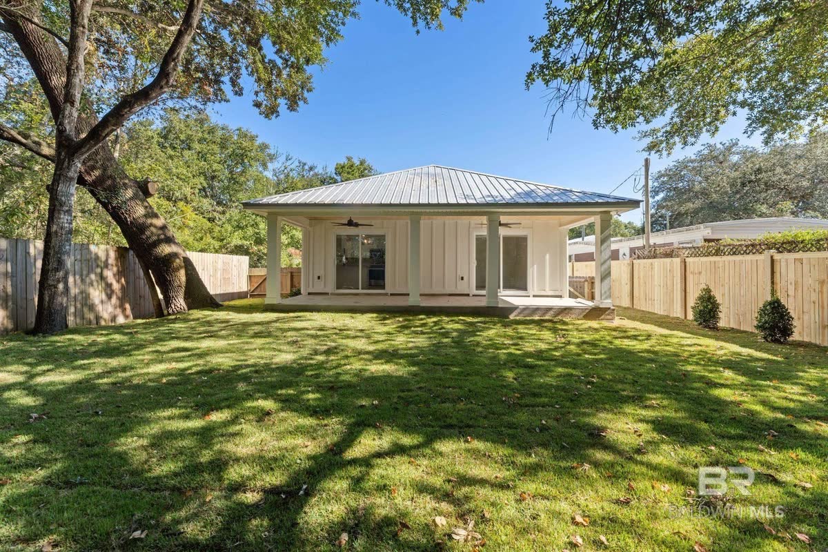 A new cottage with a metal roof seen across a wide green lawn under big trees.