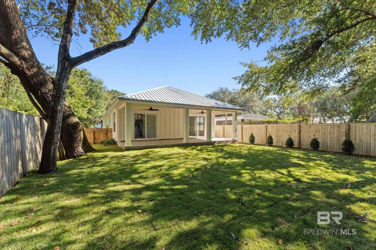 A new cottage behind a big spreading tree, a wood privacy fence around the yard.