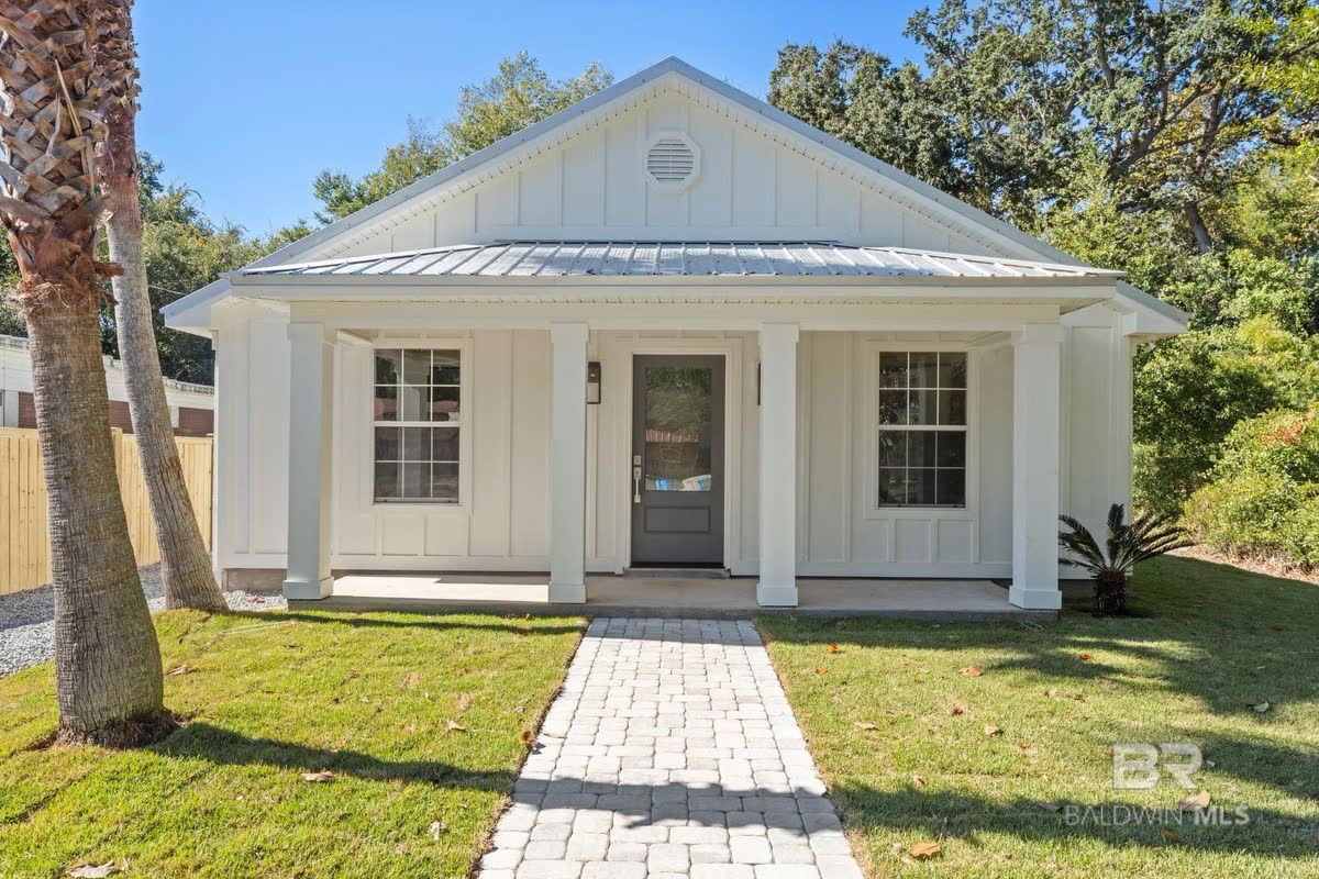 A white cottage with a metal roof and a paver walk up to a small front porch.