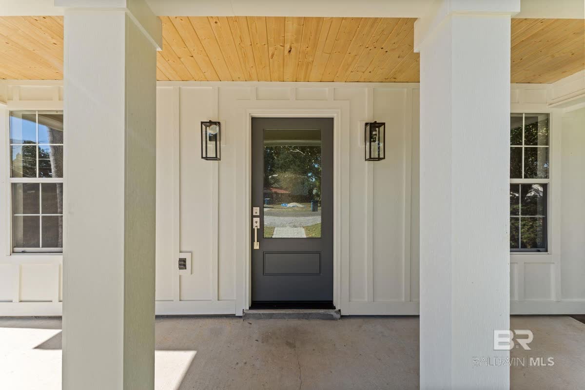 A dark front door under a wood-planked porch ceiling, black lanterns either side.