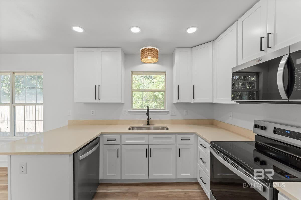 A white shaker kitchen with white counters, black hardware and a stainless range.