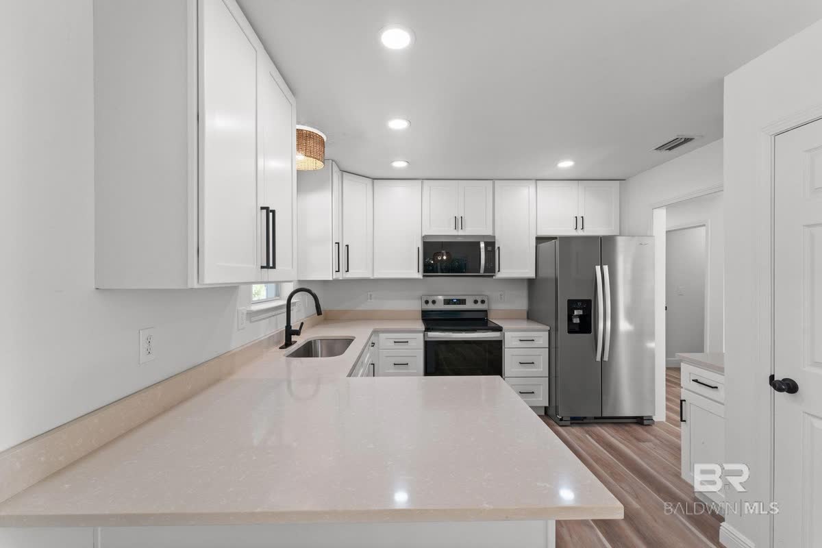 A white kitchen with a white island and a stainless refrigerator.