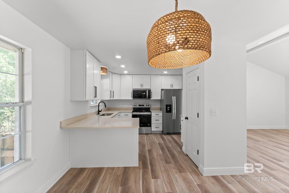 An open kitchen with white cabinets, a woven pendant light and wood-look floors.