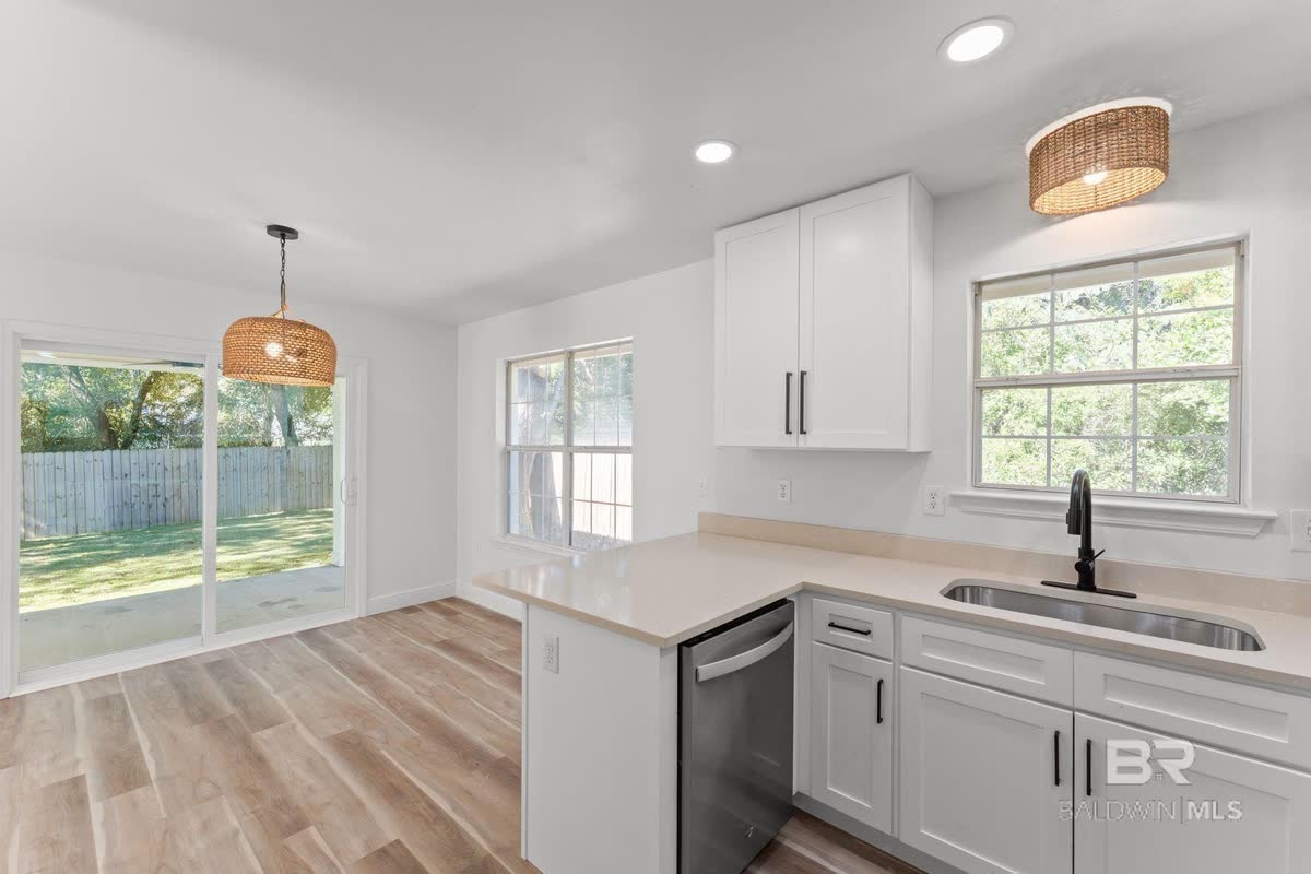 A white kitchen with a window over the sink and a woven pendant light.