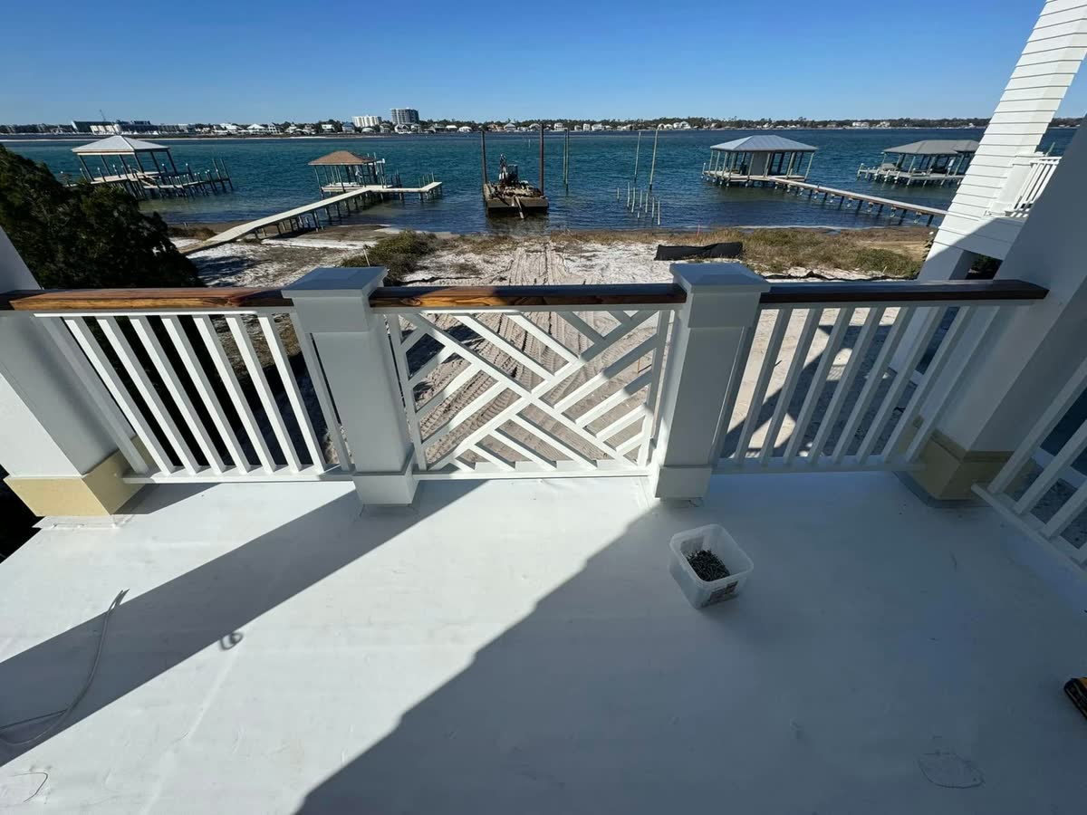 A white balcony railing with a chippendale panel and a wood cap rail, looking out over the bay.
