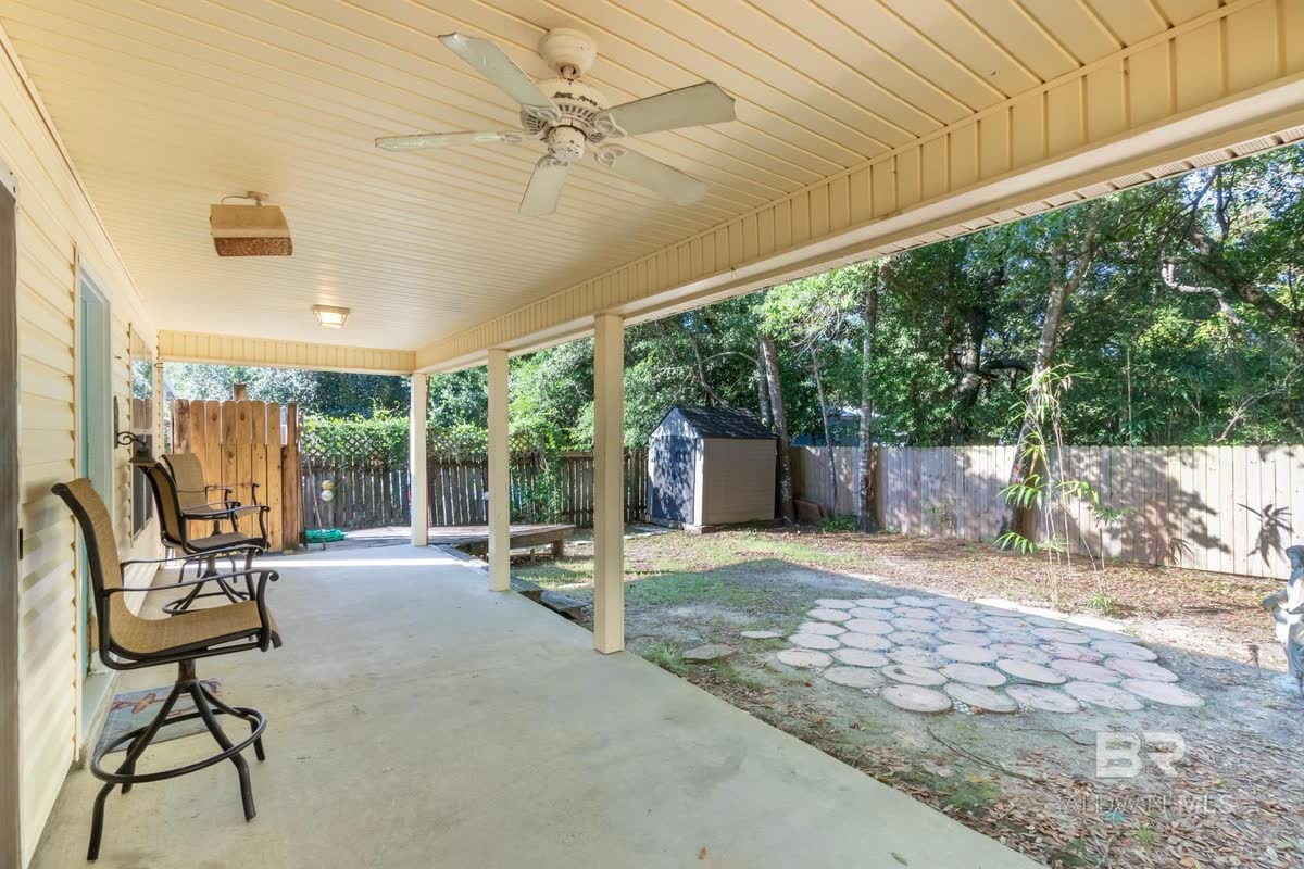 A covered back patio with a wood-planked ceiling, a ceiling fan and patio chairs.