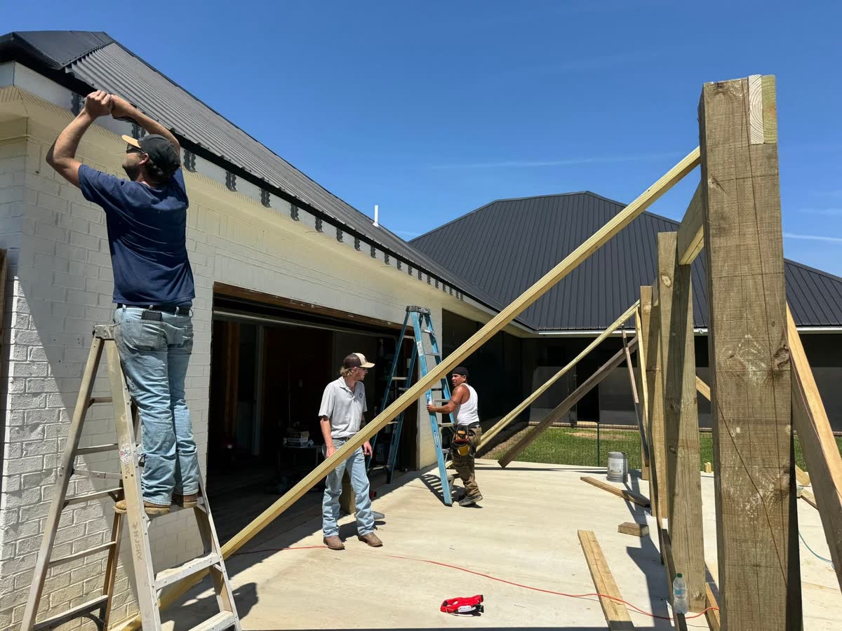 Workers framing a patio cover against the back of a brick house.