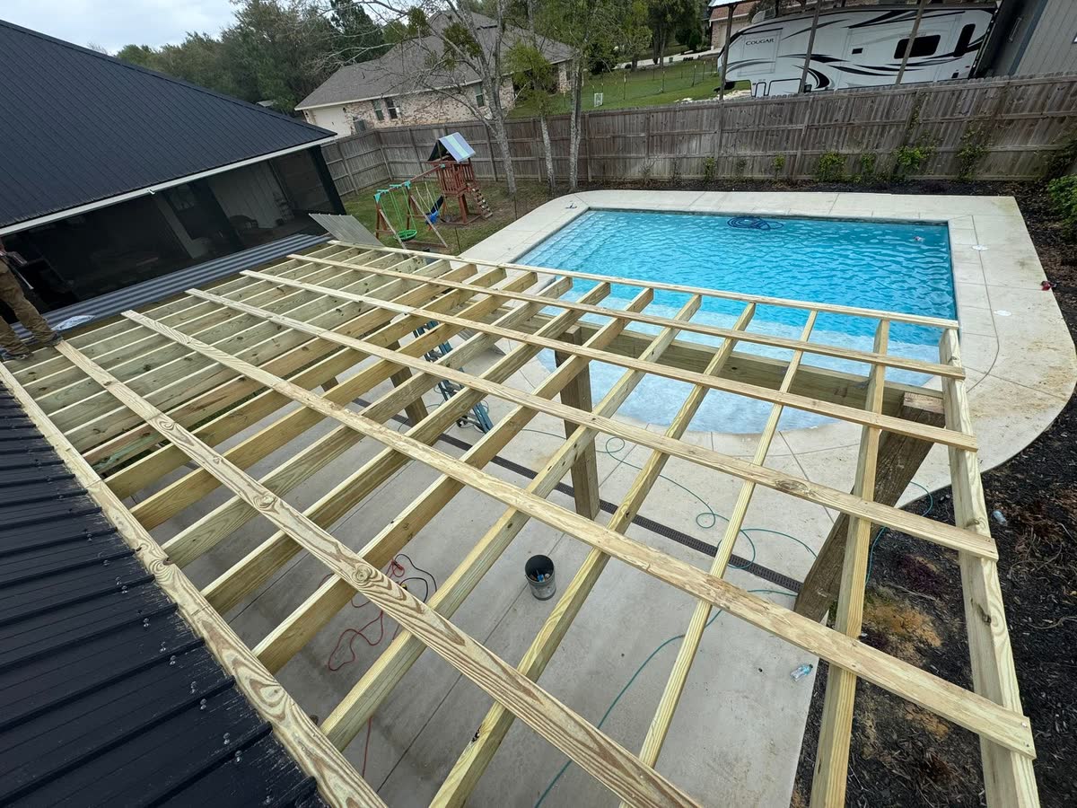 Pergola rafters framed beside a pool, seen from above.