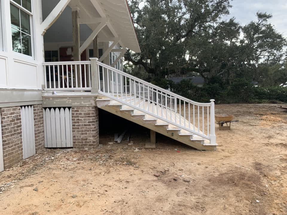 A wraparound porch with white railings on a raised brick foundation.