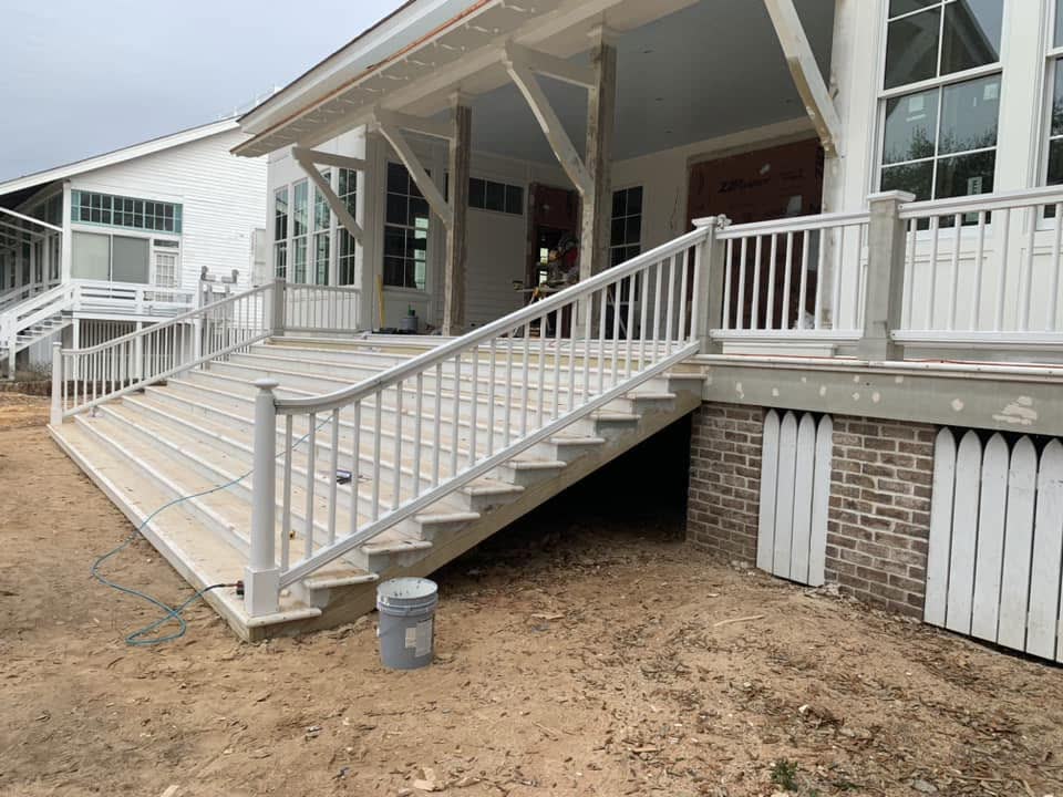 A long front porch with white railings and wide stairs down to the yard.