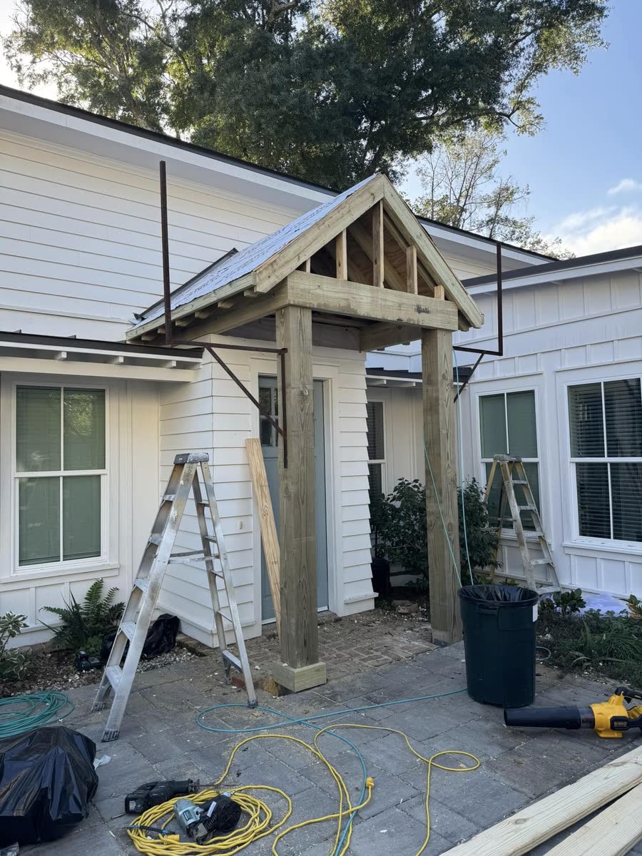 A new gabled portico with wood beams over the side door of a white house.