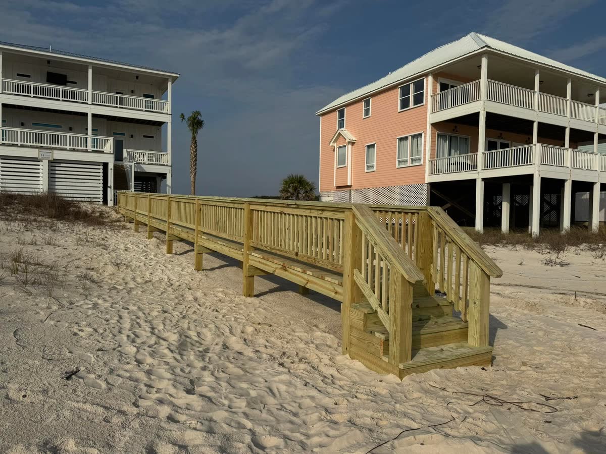 A new wooden beach walkover with stairs, raised beach houses behind it.