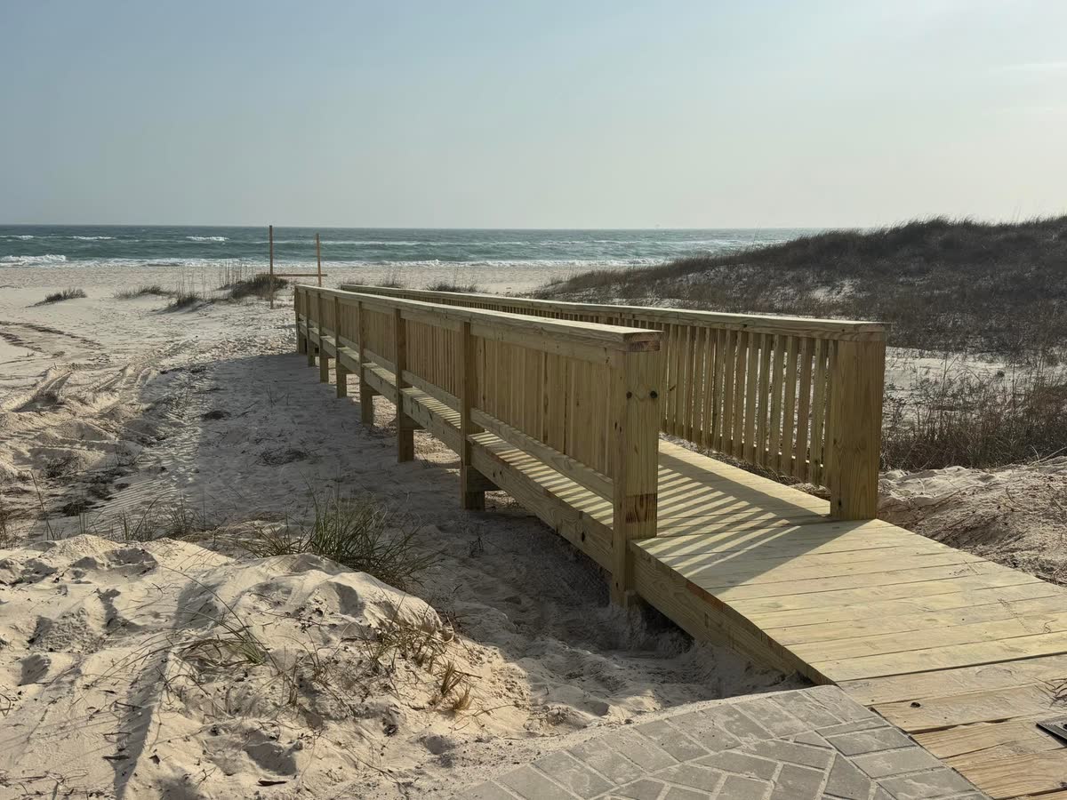 A wooden walkover with rails crossing the dune grass toward the Gulf.