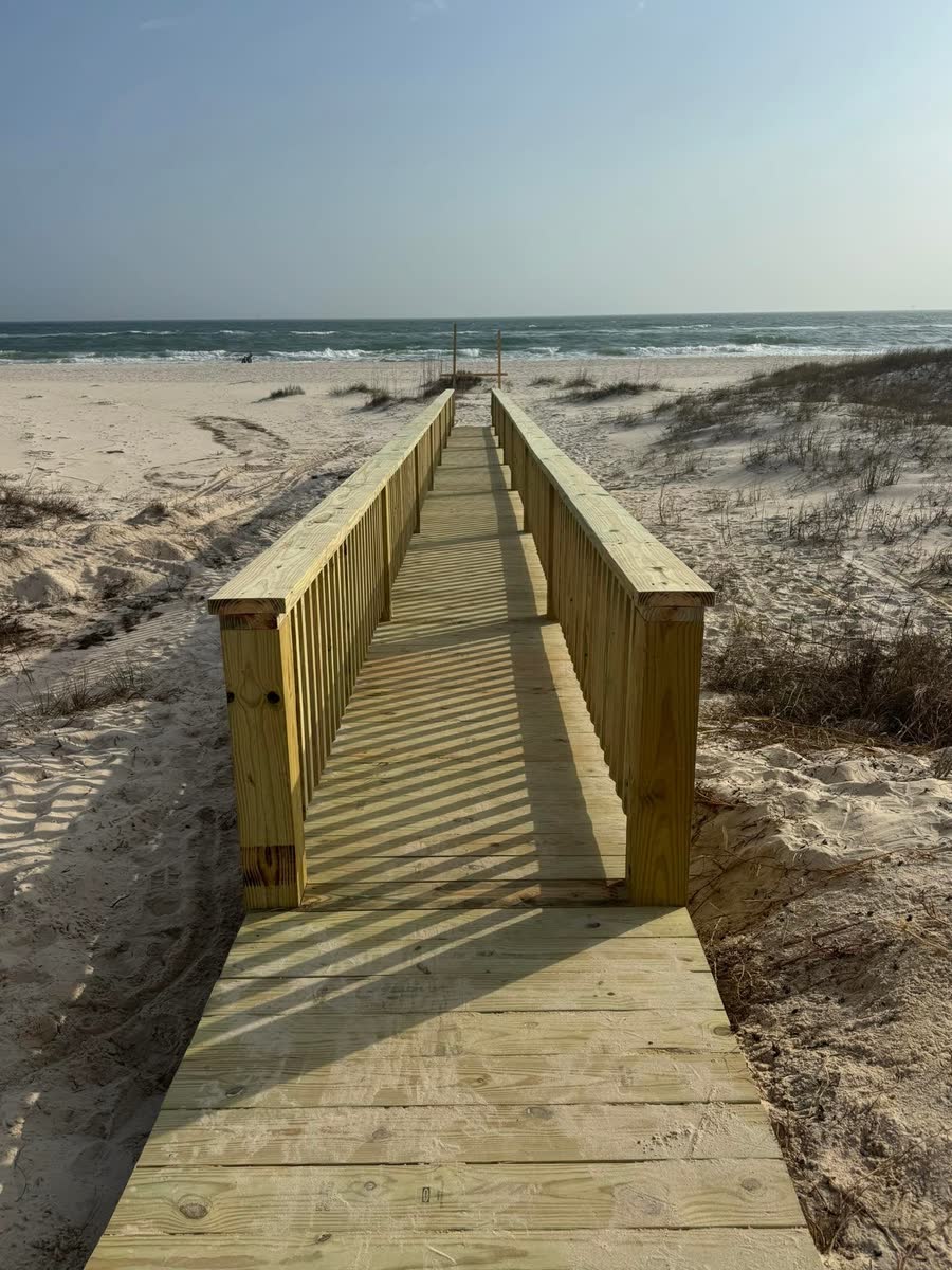 A long wooden boardwalk with rails running over the dunes to the beach.