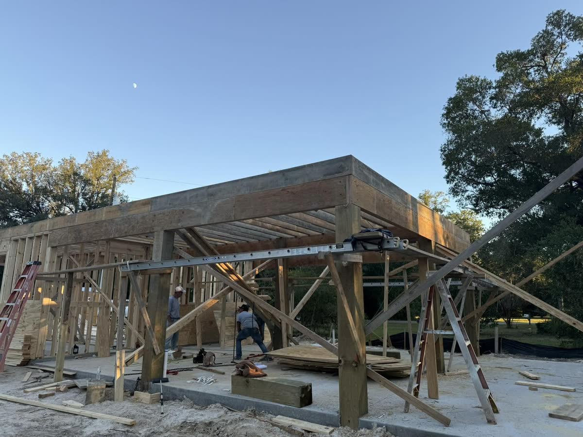 Wooden pilings with the first floor beams framed on top, two workers below.