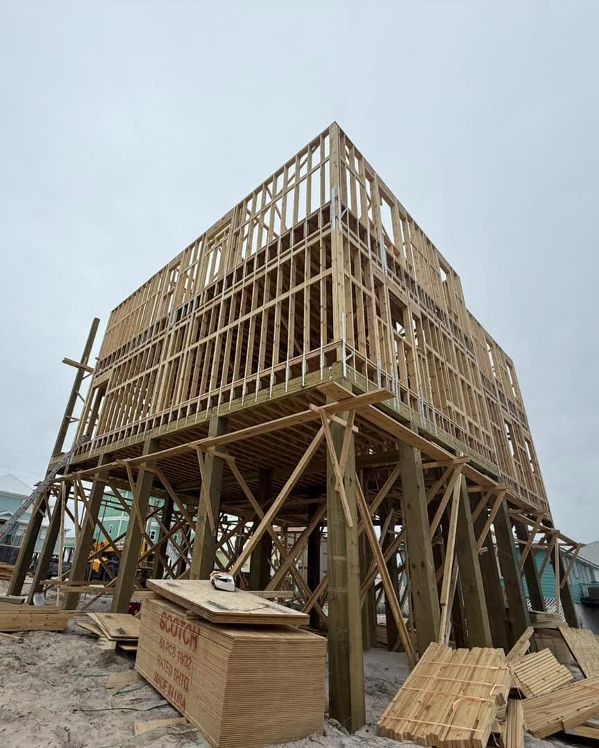 A beach house framed in raw lumber on tall wooden pilings above the sand.