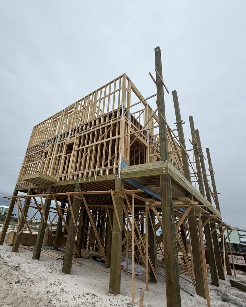 Wall framing going up on a house raised on wooden pilings and cross braces.