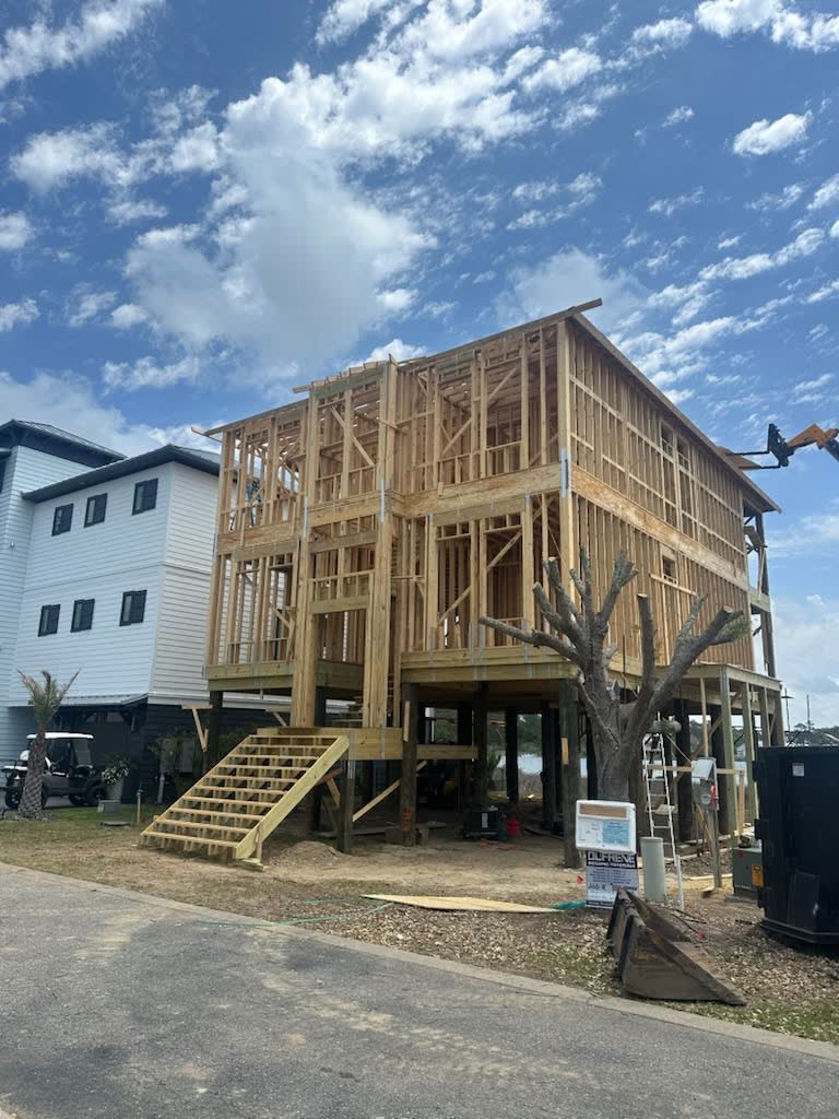 A raised house framed on pilings beside a street, a stair framed up to the first floor.