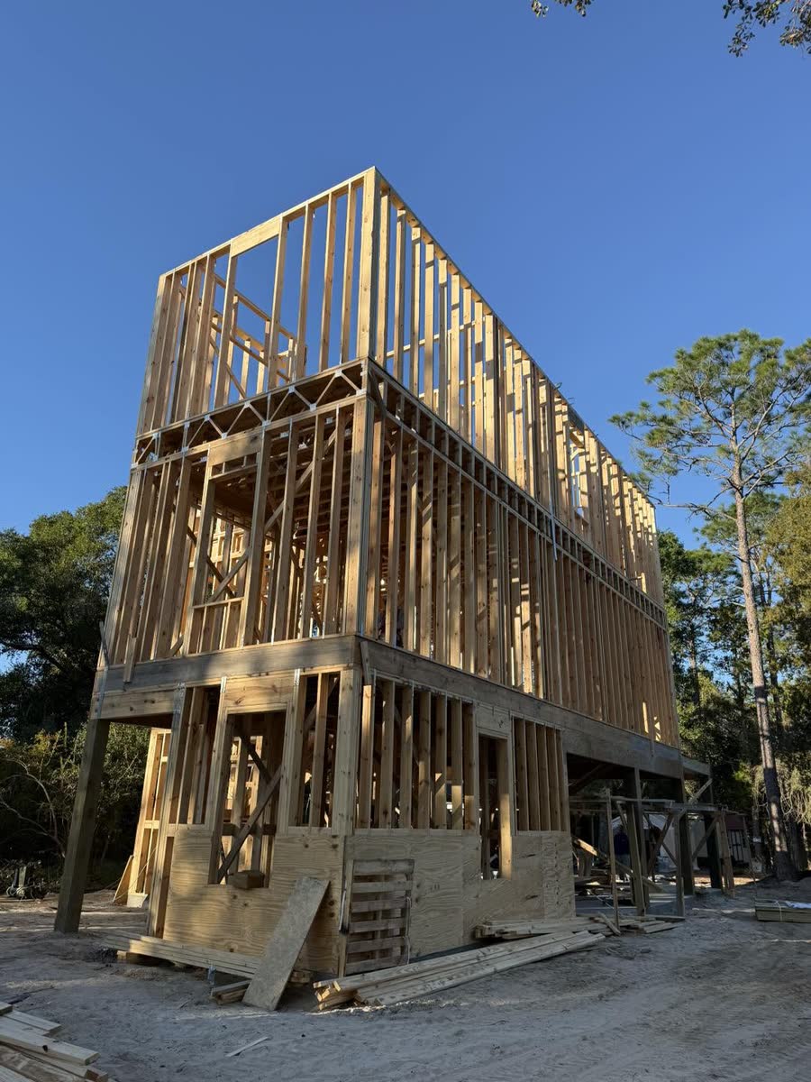 A tall raised house in raw wood framing, three floors of studs against a blue sky.