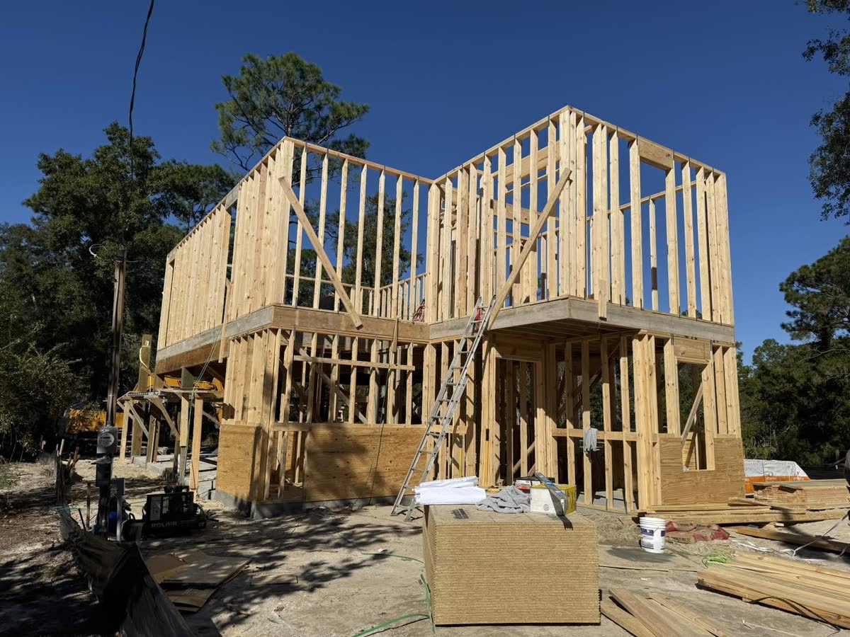 A two-storey house in raw wood framing, lumber stacked on the slab in front.