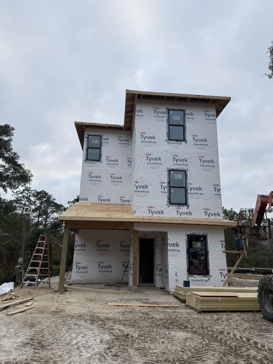 A three-storey house covered in white house wrap with the windows set in.