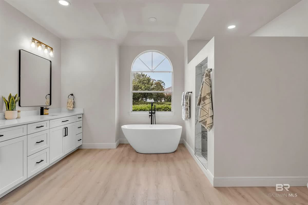 A remodeled bathroom with a double vanity, a freestanding tub and wood-look floors.
