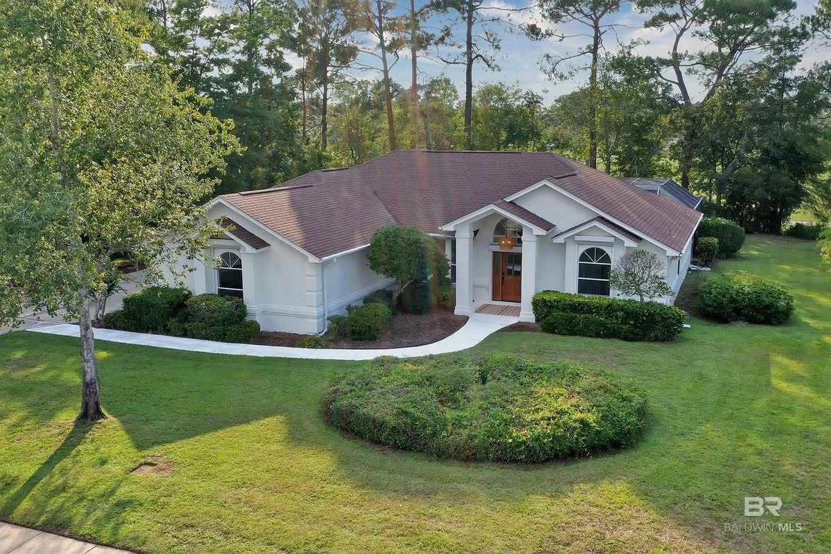 A remodeled single-storey home among pines, with a round shrub bed in the lawn.