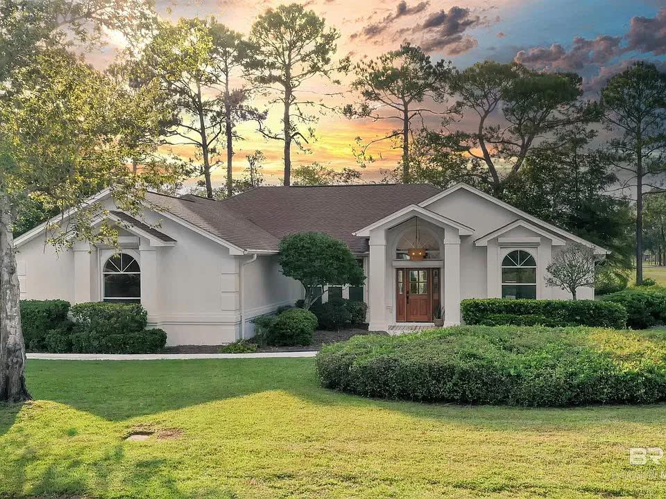 A single-storey home with a hipped roof and an arched wood front door, at dusk.