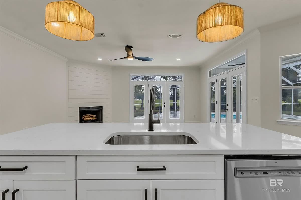 A remodeled white kitchen with a white island, a woven pendant light and French doors.