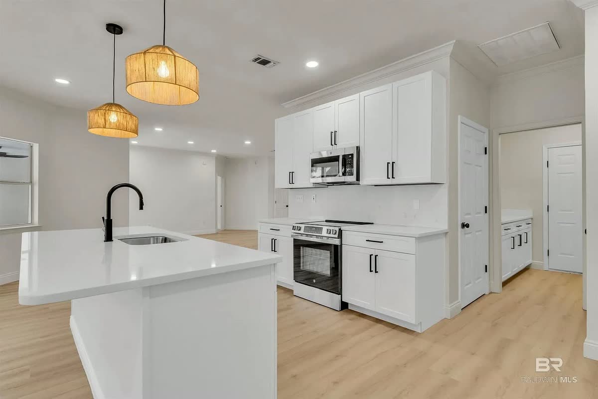 A remodeled white kitchen with two woven pendant lights over the island, shaker cabinets and a stainless range.